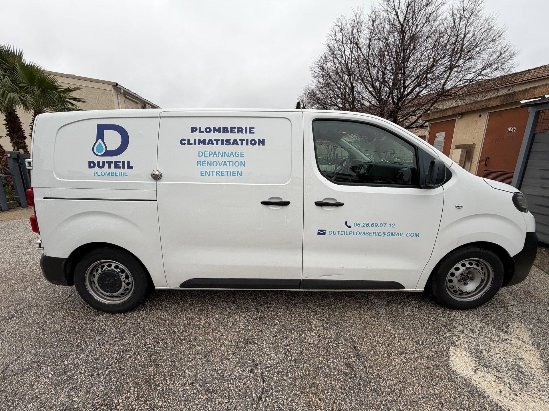 Camionnette blanche portant l'inscription « DUTIL Plomberie Climatisation » garée devant un bâtiment.