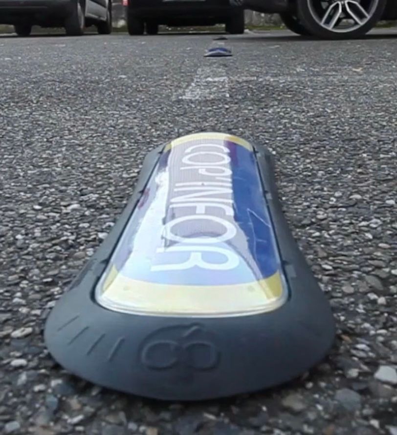 panneaux de stationnement gris sur l'asphalte, portant l'inscription « COPINFOR ». Voitures en arrière-plan.