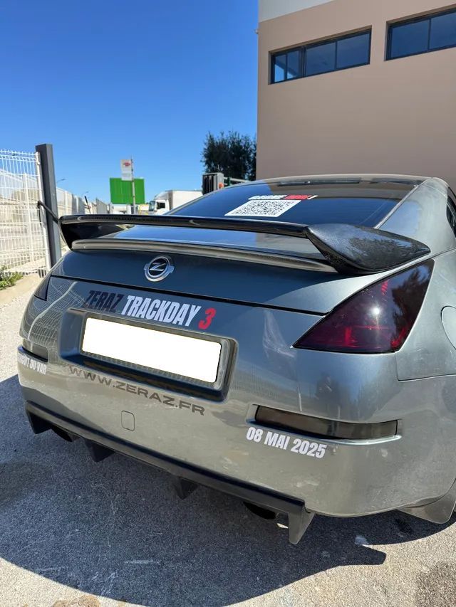 Nissan 350Z grise avec aileron sur circuit, sous un ciel dégagé.