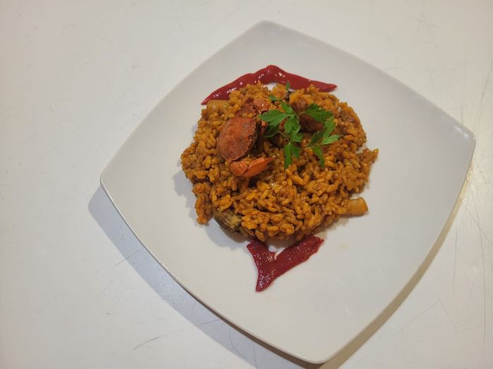 Un plato de paella cubierto con chorizo y una ramita de perejil, adornado con dos tiras de pimiento rojo.