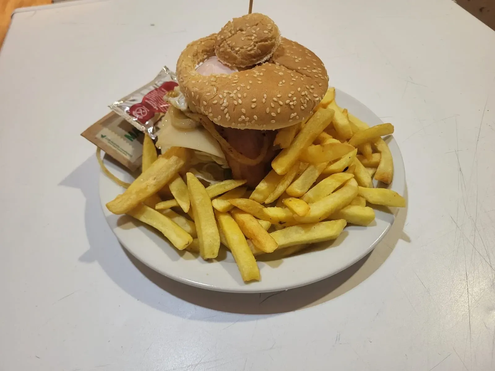 Hamburguesa con papas fritas en un plato; paquetes de ketchup; pan, hamburguesa y lechuga son visibles.
