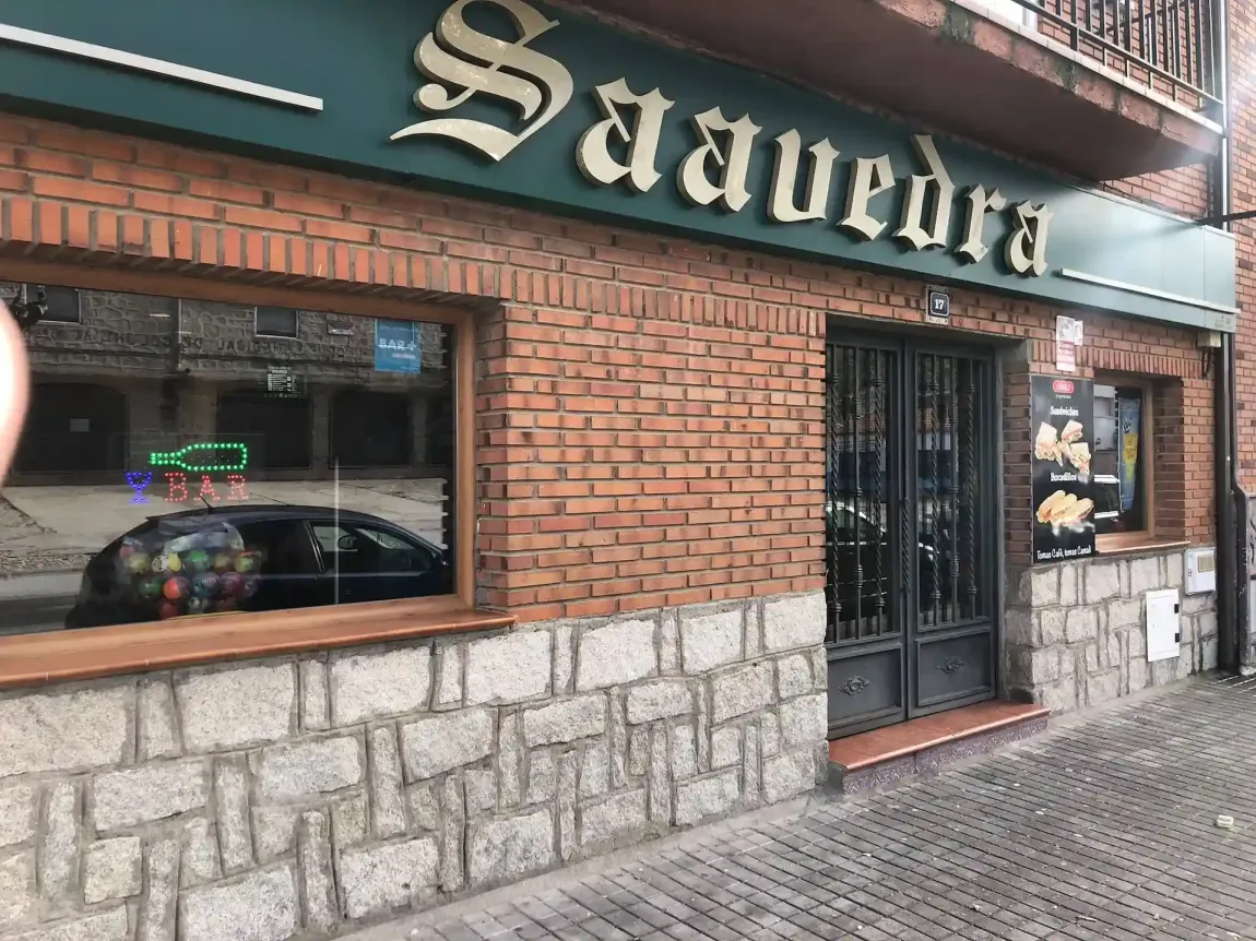 La fachada de ladrillo y piedra de un restaurante llamado Saavedra, con un letrero verde oscuro y grandes escaparates, da a una calle.