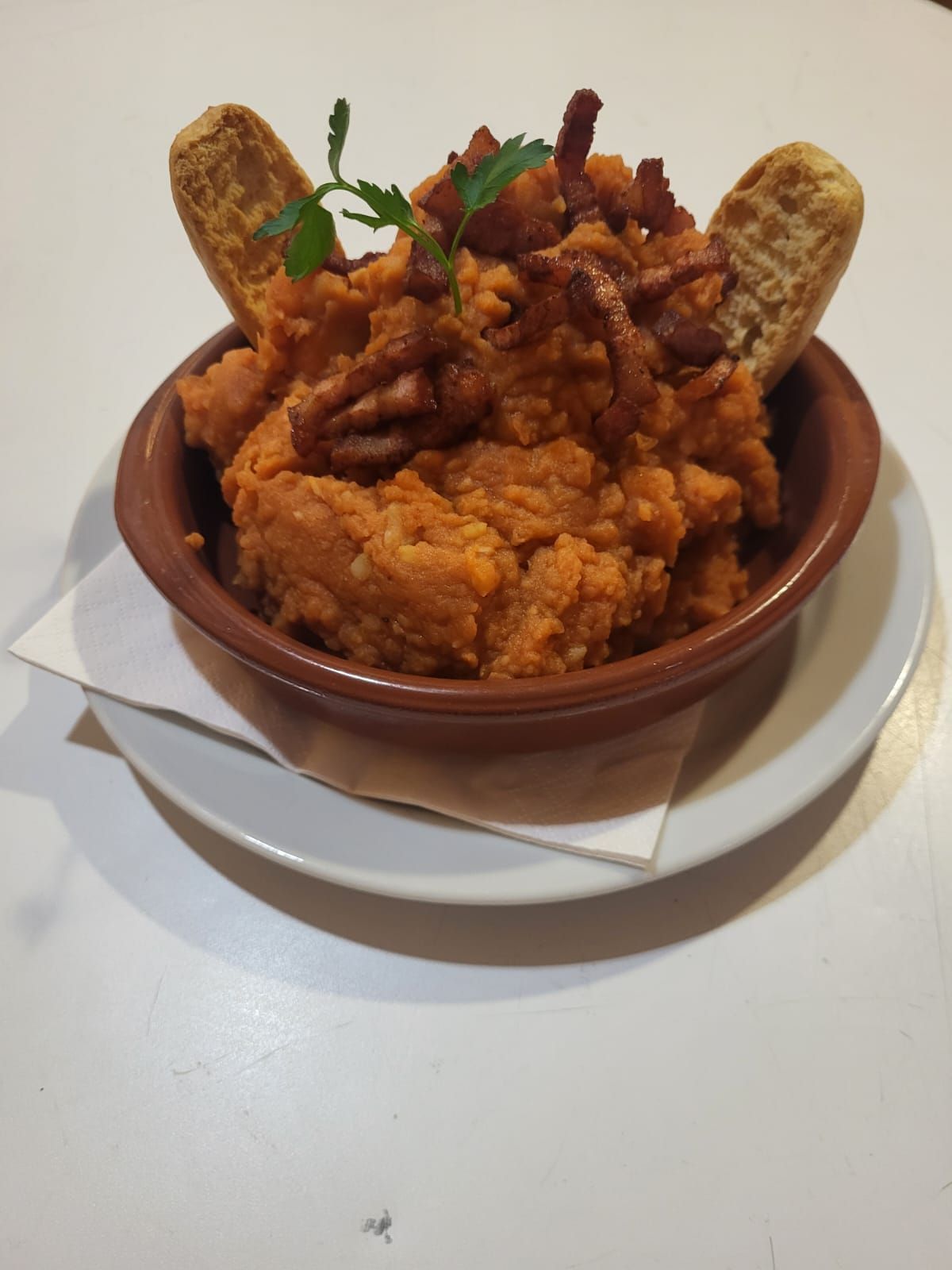 Cuenco de puré de naranja cubierto con tocino y crutones, en un plato.