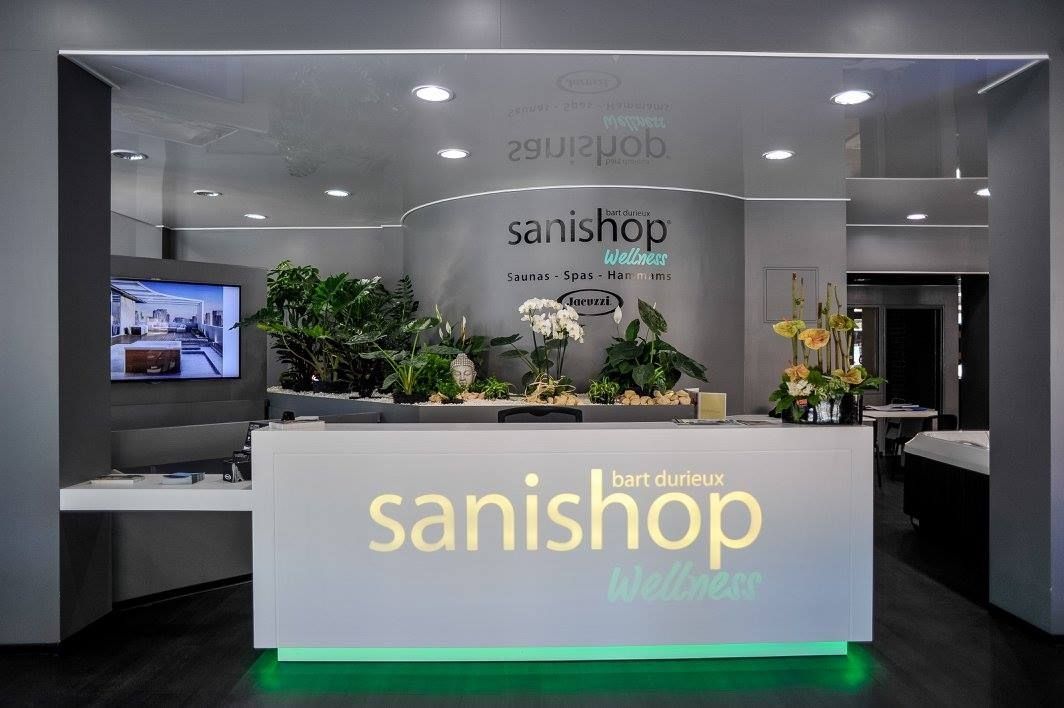 Comptoir d'accueil d'un magasin Sanishop avec éclairage d'ambiance vert et présentoir à plantes.
