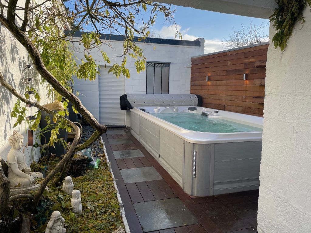 Spa extérieur avec revêtement gris, jouxtant une terrasse en bois et des murs blancs.