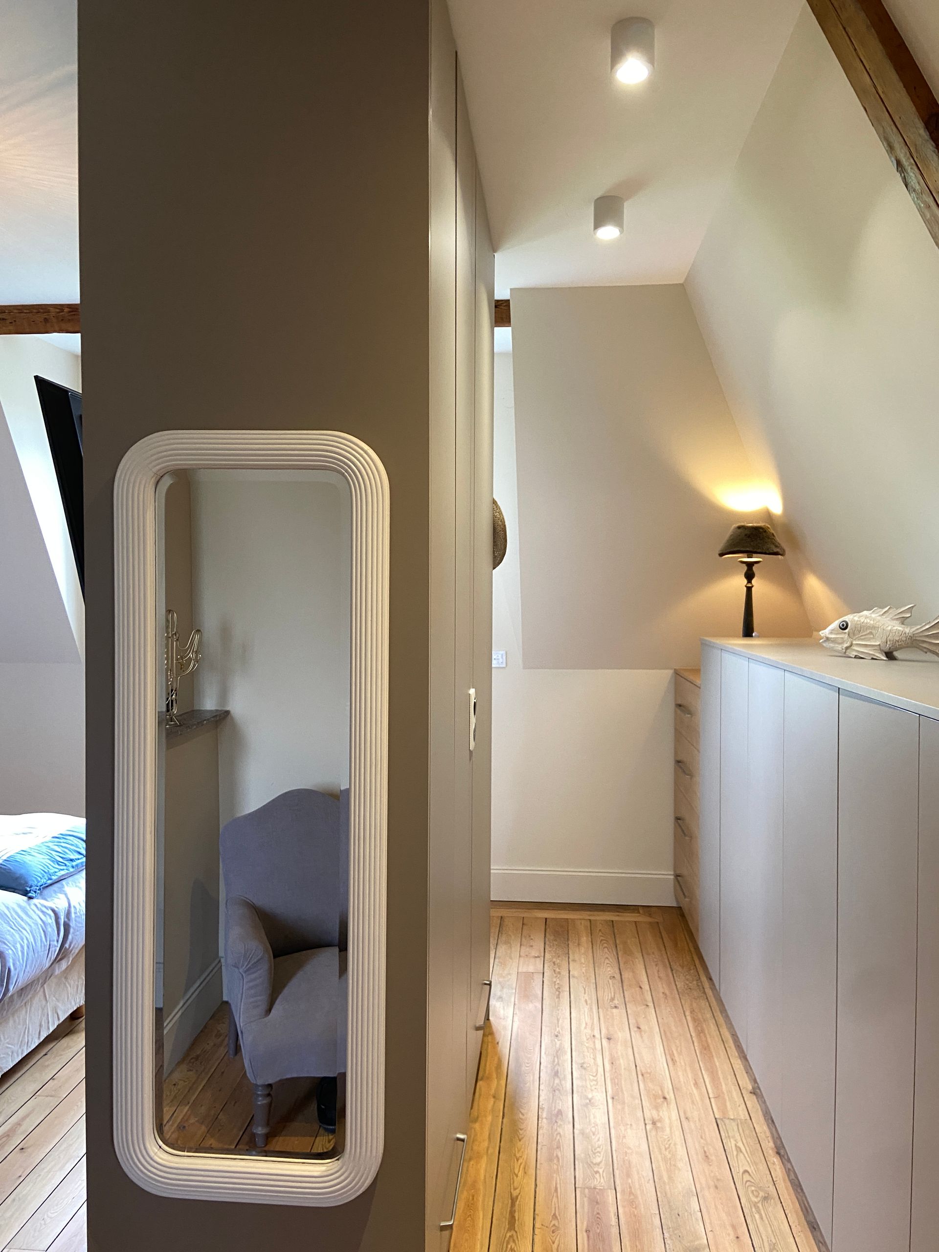 Long couloir avec miroir à cadre blanc, rangements intégrés et plafond en pente ; sol en bois.