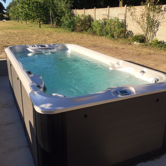 Spa de nage rectangulaire rempli d'eau bleue, en extérieur par une journée ensoleillée.