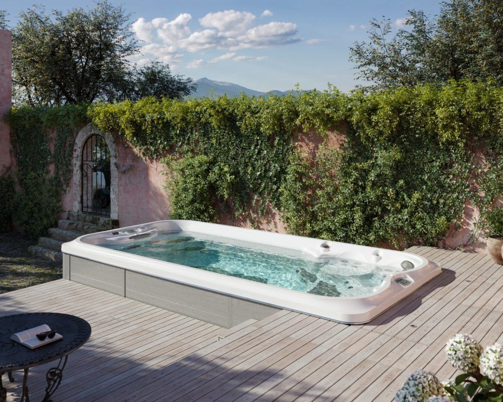 Spa de nage sur une terrasse en bois entourée de verdure, dans un cadre extérieur ensoleillé.