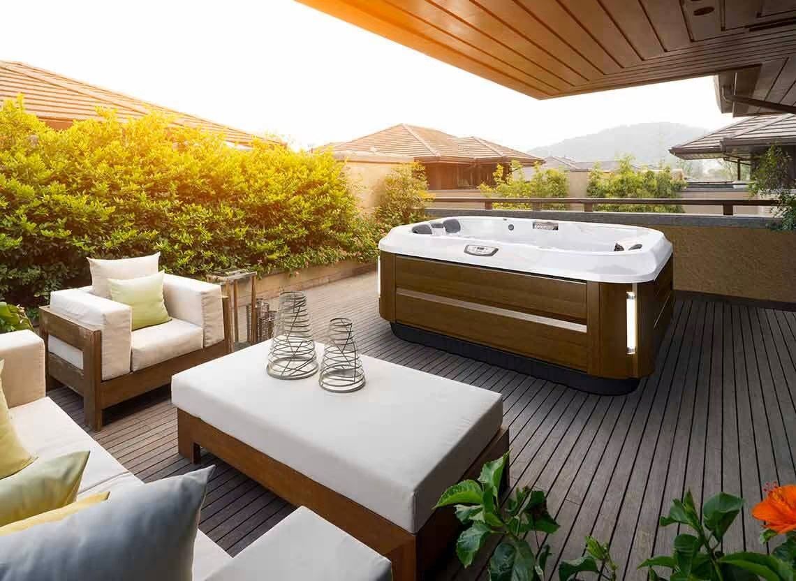 Jacuzzi extérieur sur une terrasse en bois avec coin salon et végétation environnante.