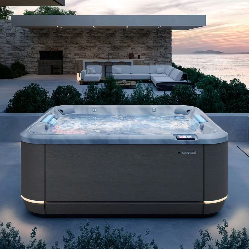Jacuzzi sur une terrasse donnant sur l'océan ; tons gris et beige, éclairé par des lumières bleues.