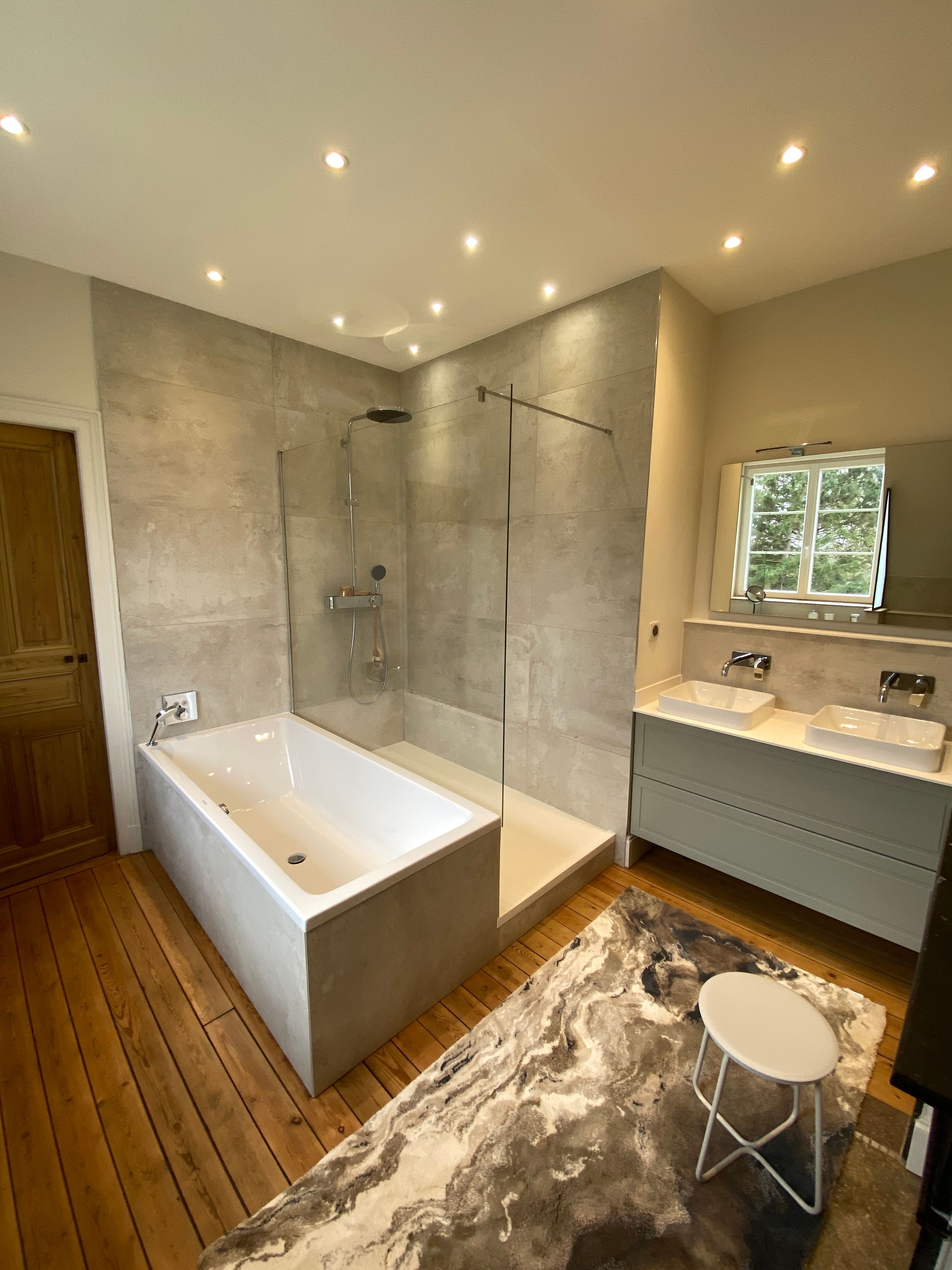 Salle de bains moderne avec douche et baignoire carrelées grises, parquet et double vasque.