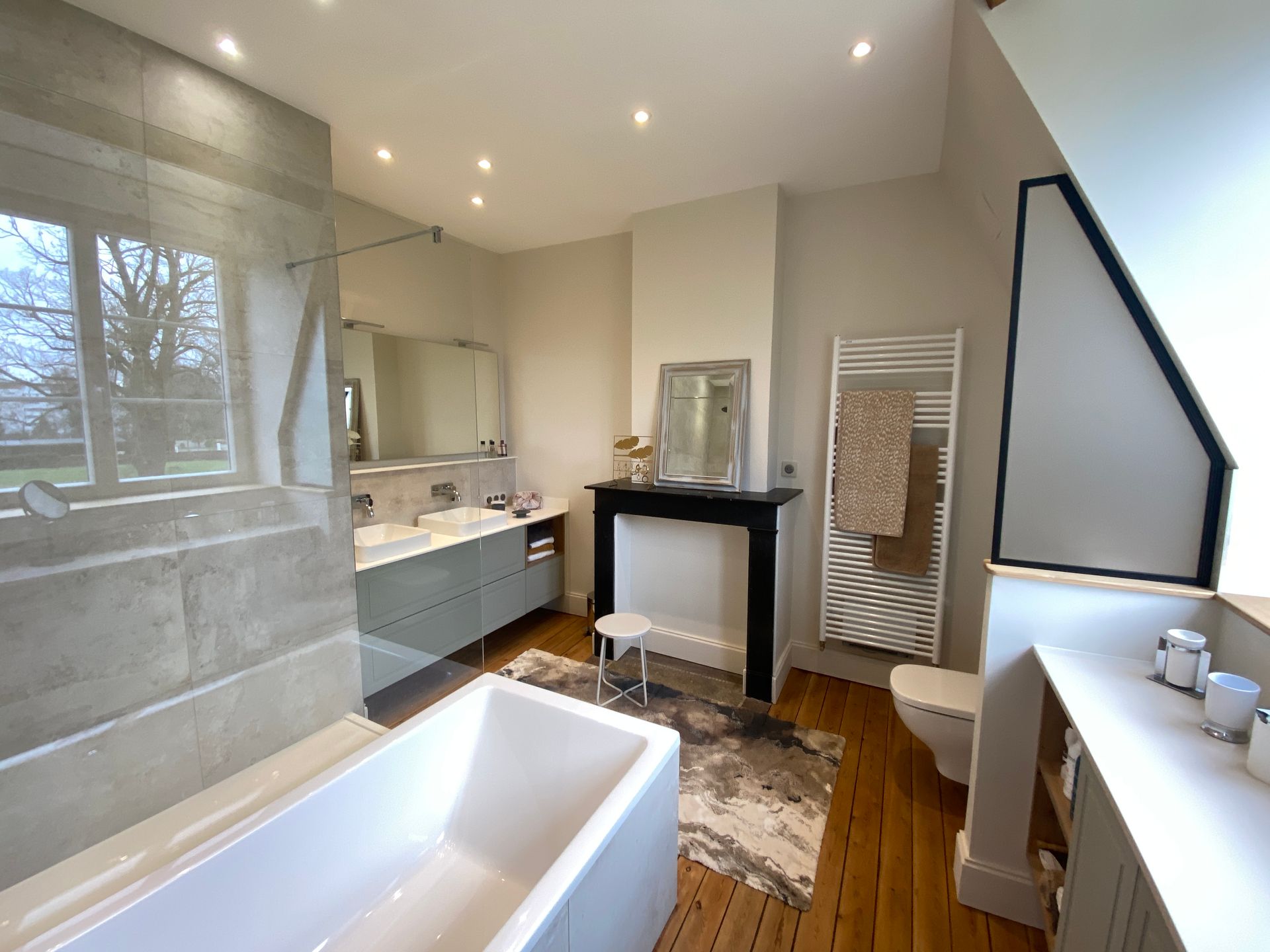 Salle de bains moderne avec baignoire, meuble-lavabo, cheminée et sèche-serviettes chauffant.