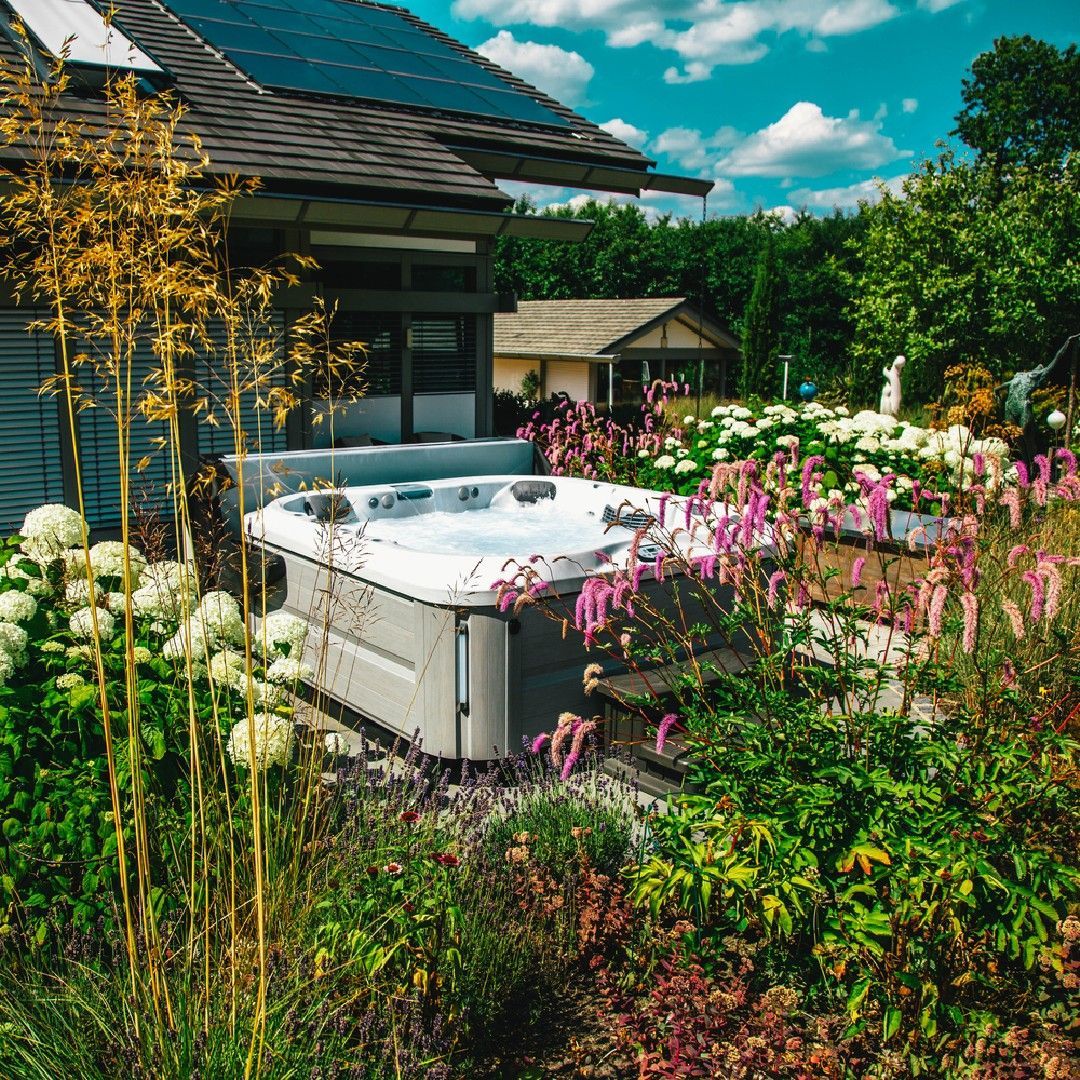 Un jacuzzi se dresse dans un jardin luxuriant, à côté d'une maison équipée de panneaux solaires.