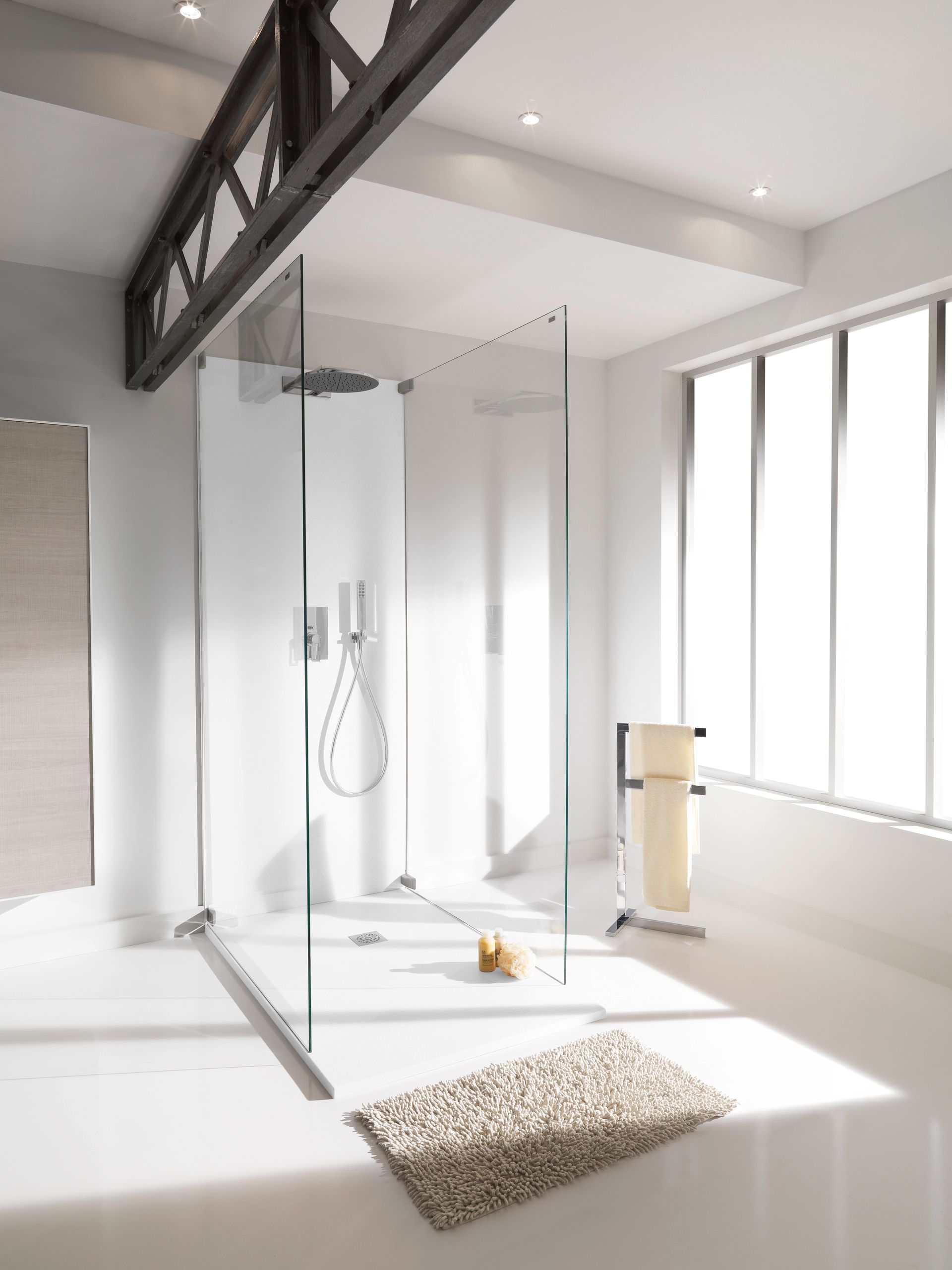 Salle de bains moderne avec douche en verre, murs blancs et poutre industrielle.