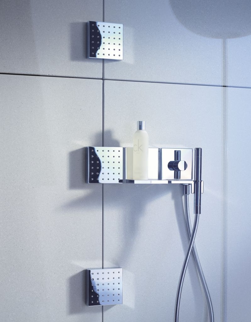 Robinetterie de douche chromée sur un mur carrelé avec une étagère supportant une bouteille.