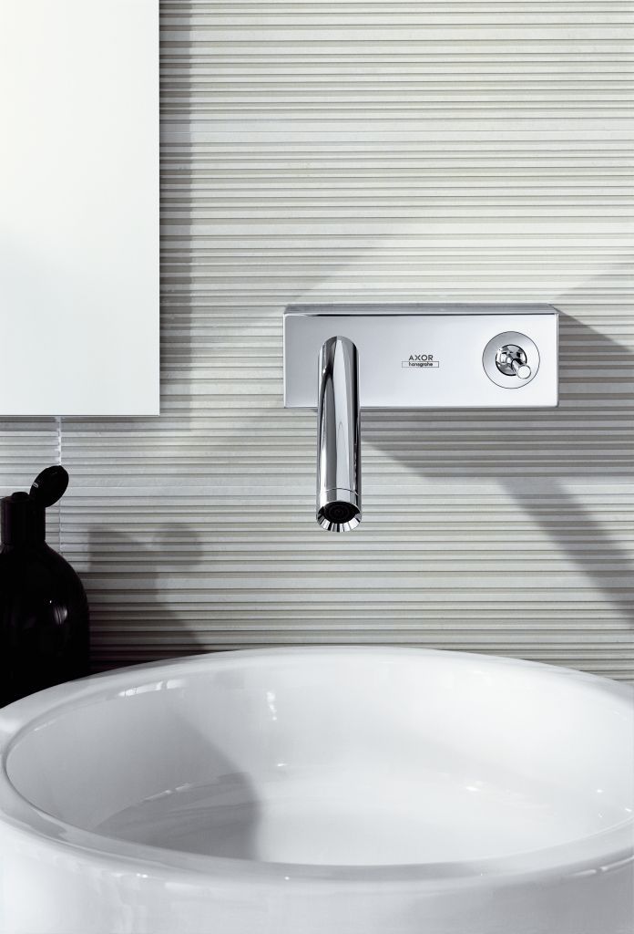 Robinet et lavabo chromés contre un mur texturé. Lavabo blanc arrondi sous un robinet chromé.