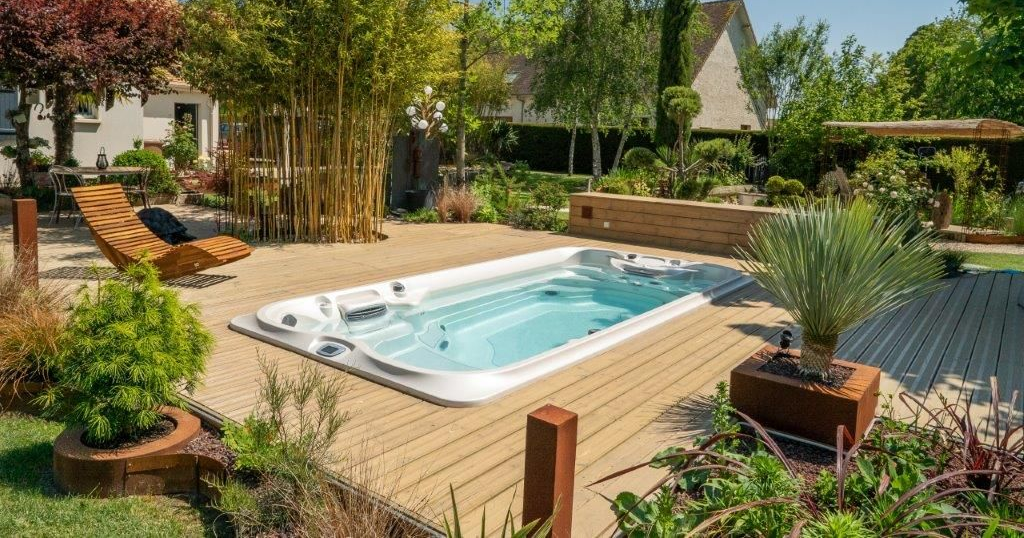 Cour arrière avec un spa de nage rectangulaire entouré d'une terrasse en bois et d'aménagements paysagers.