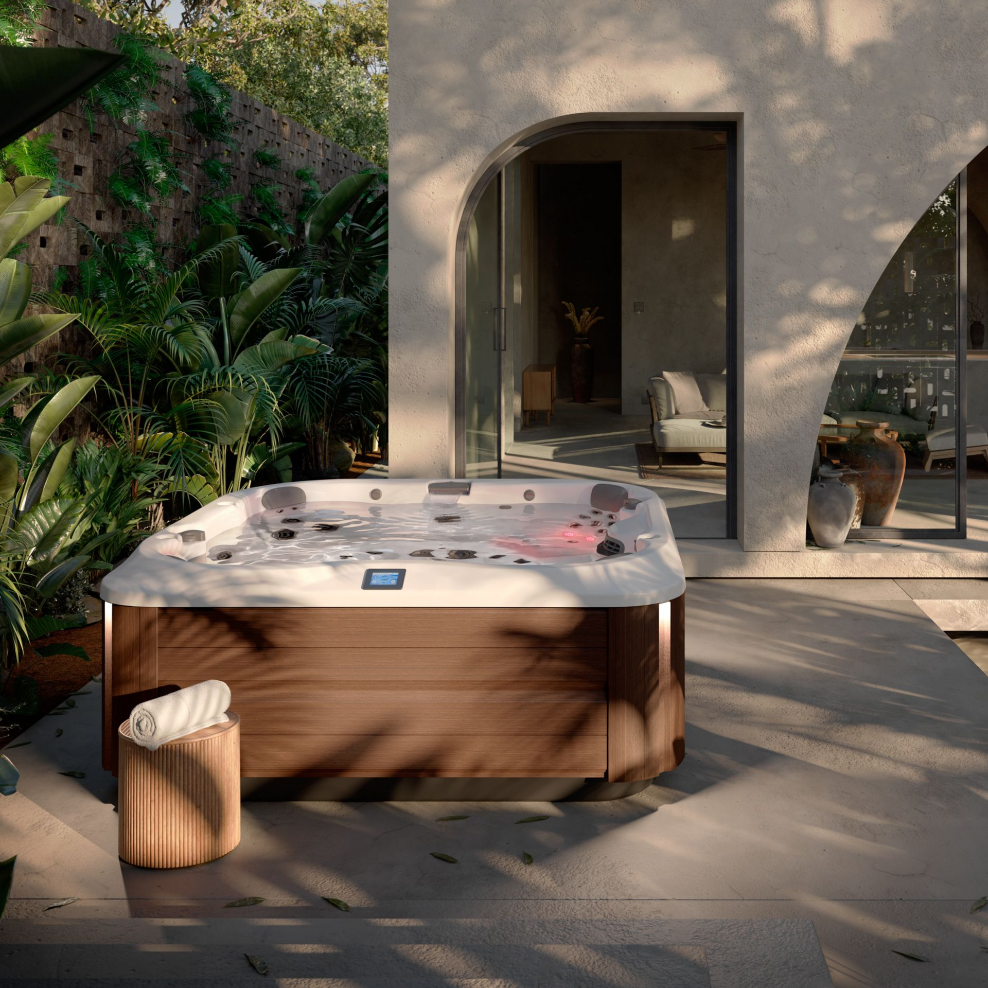 Jacuzzi sur une terrasse avec serviettes, végétation luxuriante et porte cintrée.