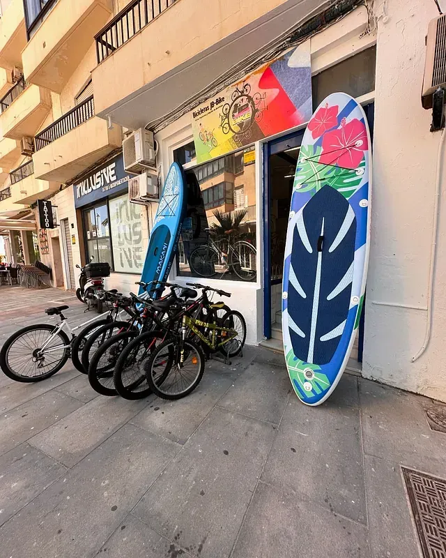 Una fila de bicicletas y tablas de surf están estacionadas afuera de una tienda.