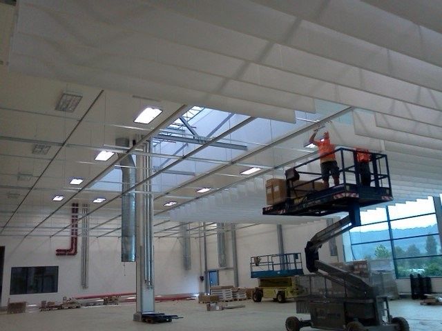 Hände halten eine Skizze für eine Inneneinrichtung und Holzproben; im Hintergrund sind ein Laptop und eine Farbpalette zu sehen.