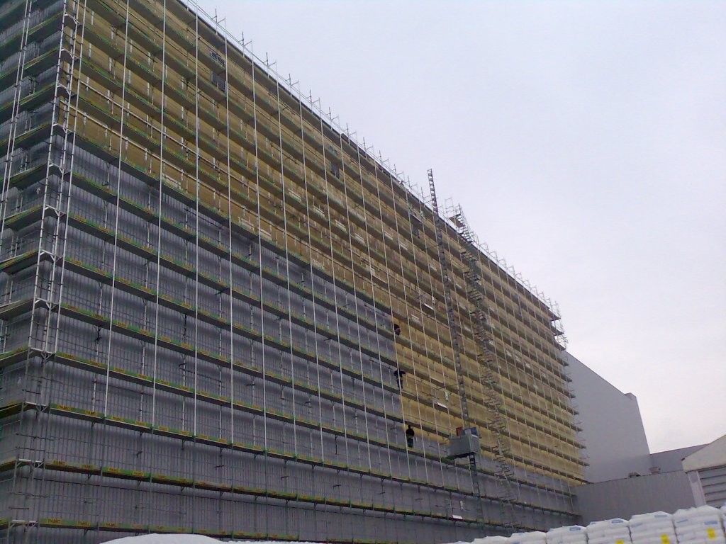 Modernes, grau-weißes Apartmentgebäude mit Balkonen, Bäumen und blauem Himmel.