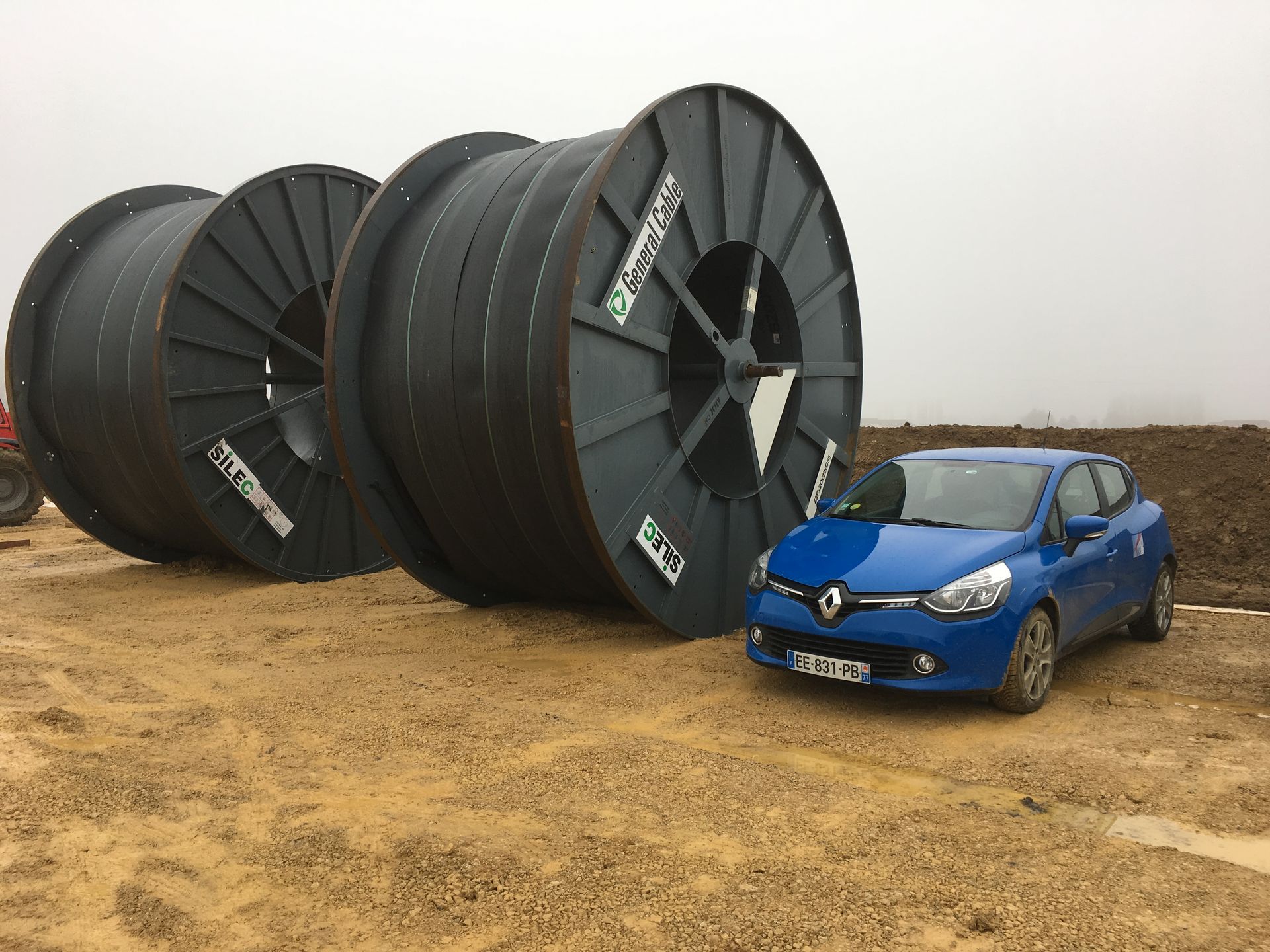Véhicule bleu garé à côté de grandes bobines noires.
