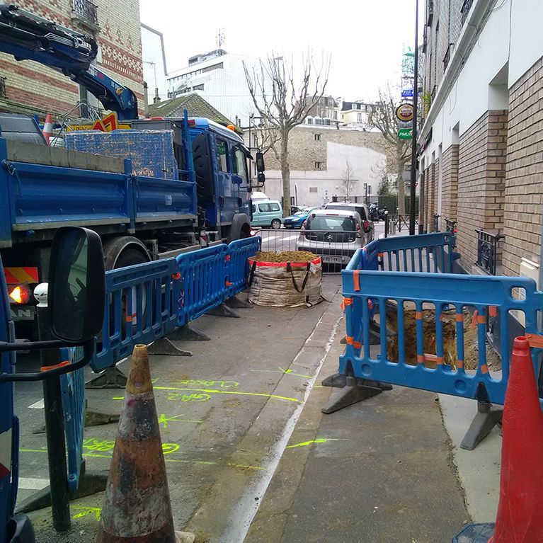 Véhicule stationné sur la route à proximité d'un chantier délimité par des barrières bleues.