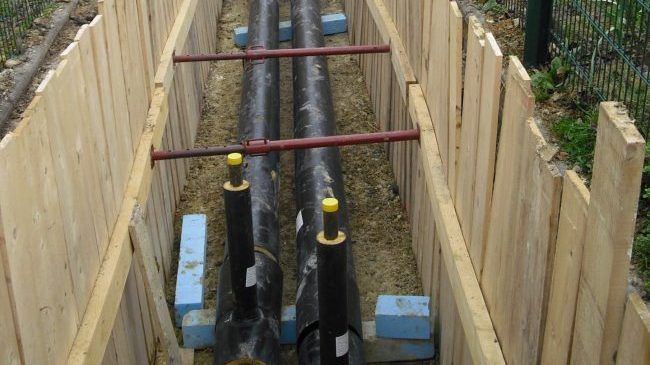 Conduites dans une tranchée aux murs recouverts de planches de bois.