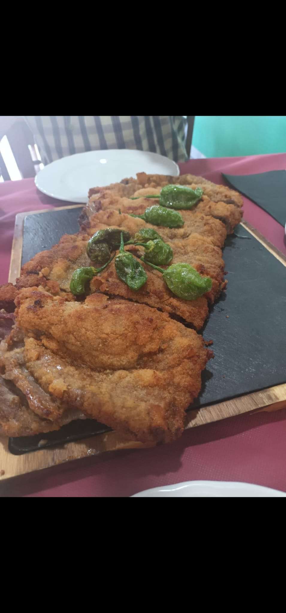 Interior de restaurante con mesas y sillas de madera, paredes de piedra y suelo de baldosas.