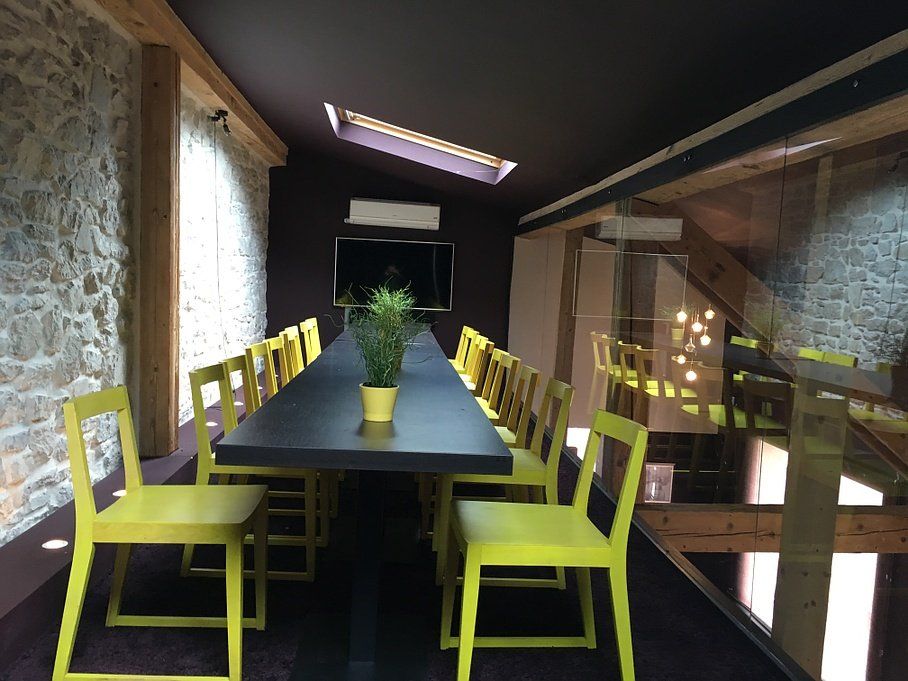 Une salle avec une longue table noire et des chaises vertes