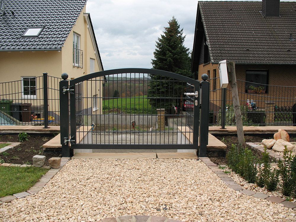 Ein schwarzes Tor ist zu einer Kiesauffahrt vor einem Haus geöffnet