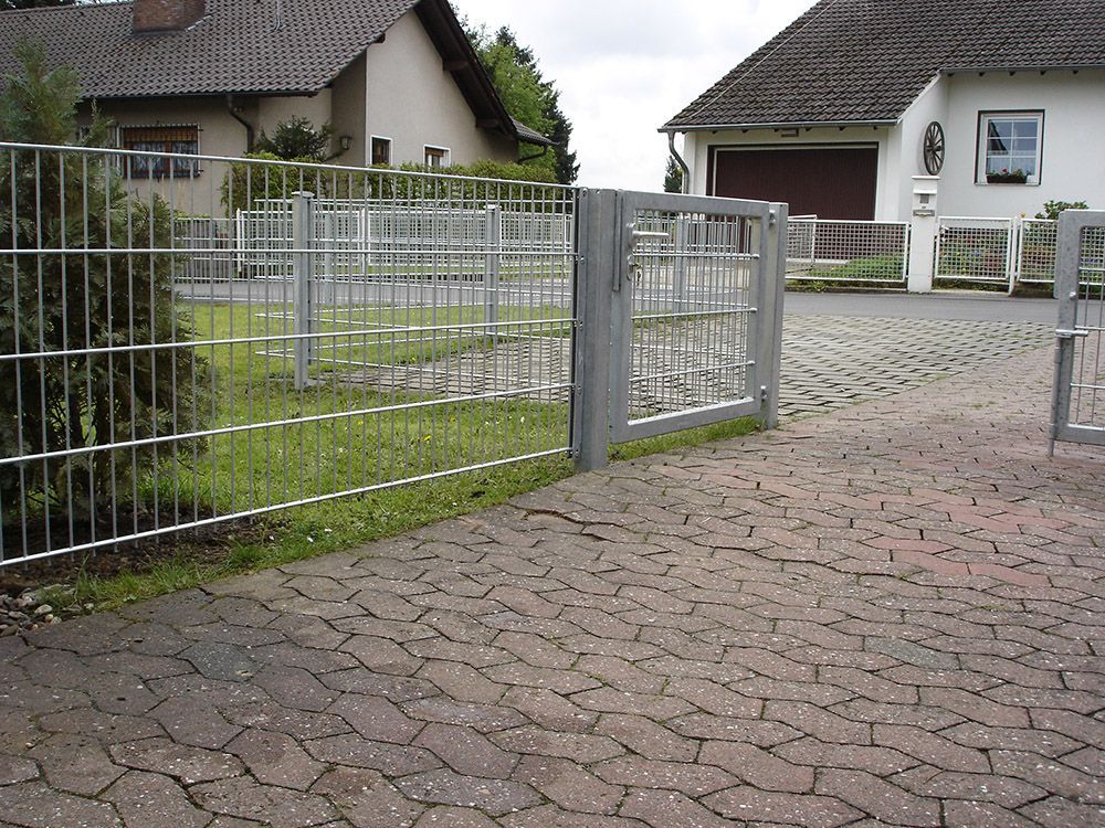 Ein Metallzaun umgibt eine gemauerte Auffahrt vor einem Haus