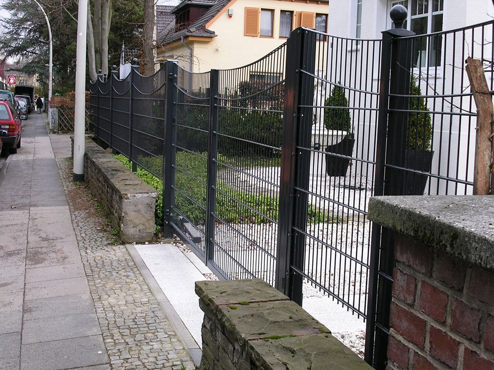 Ein schwarzer Zaun umgibt eine Backsteinmauer vor einem Haus