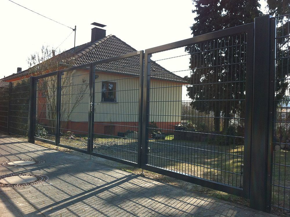 Ein Zaun umgibt ein Haus mit einer gemauerten Auffahrt davor