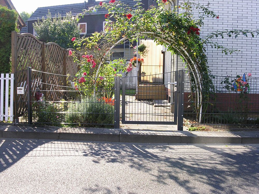 Ein weißes Backsteinhaus mit einem Tor, umgeben von Blumen