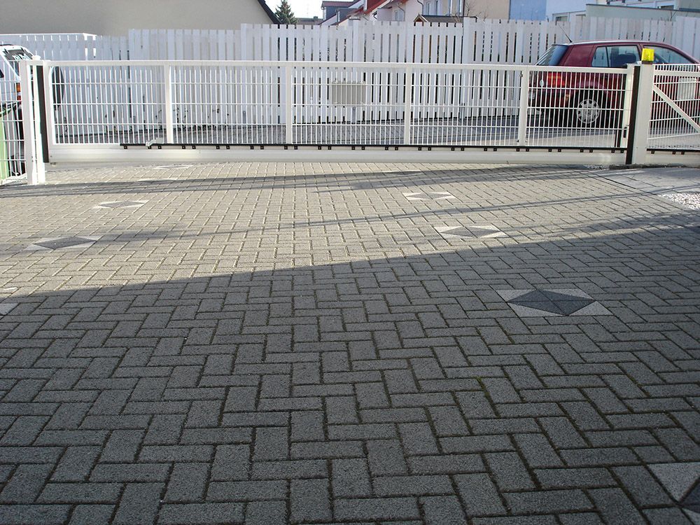 Eine gemauerte Auffahrt mit einem weißen Zaun im Hintergrund