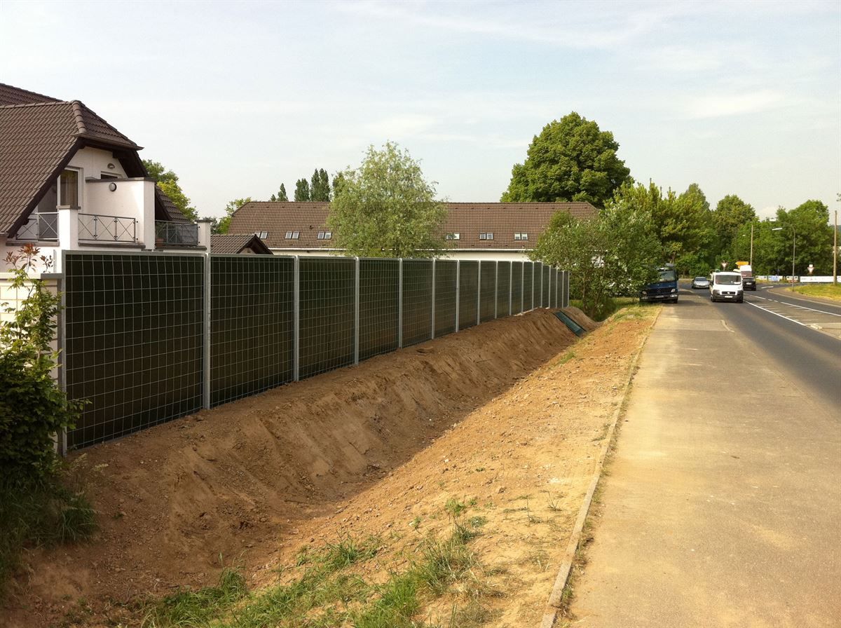 Ein Zaun am Straßenrand mit einem Haus im Hintergrund