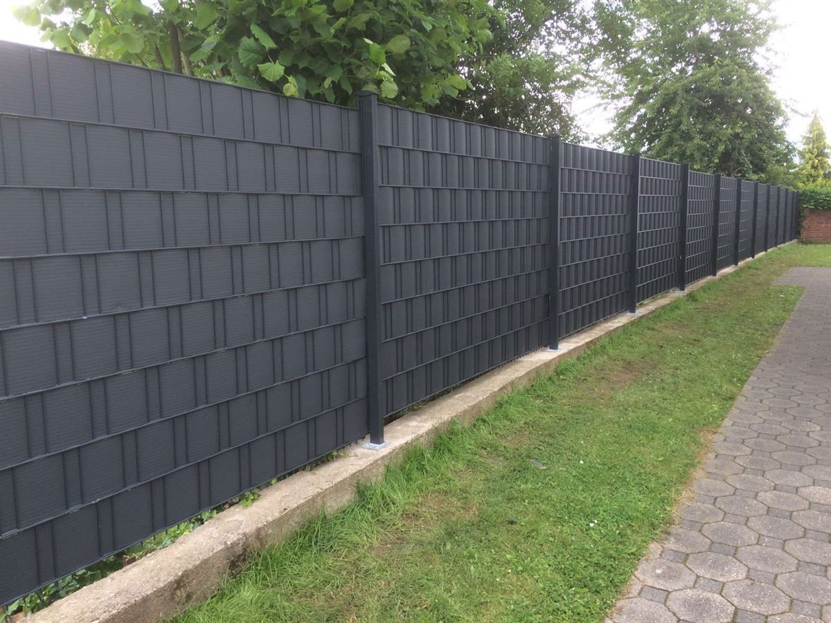 Ein schwarzer Zaun mit einem gemauerten Gehweg dahinter