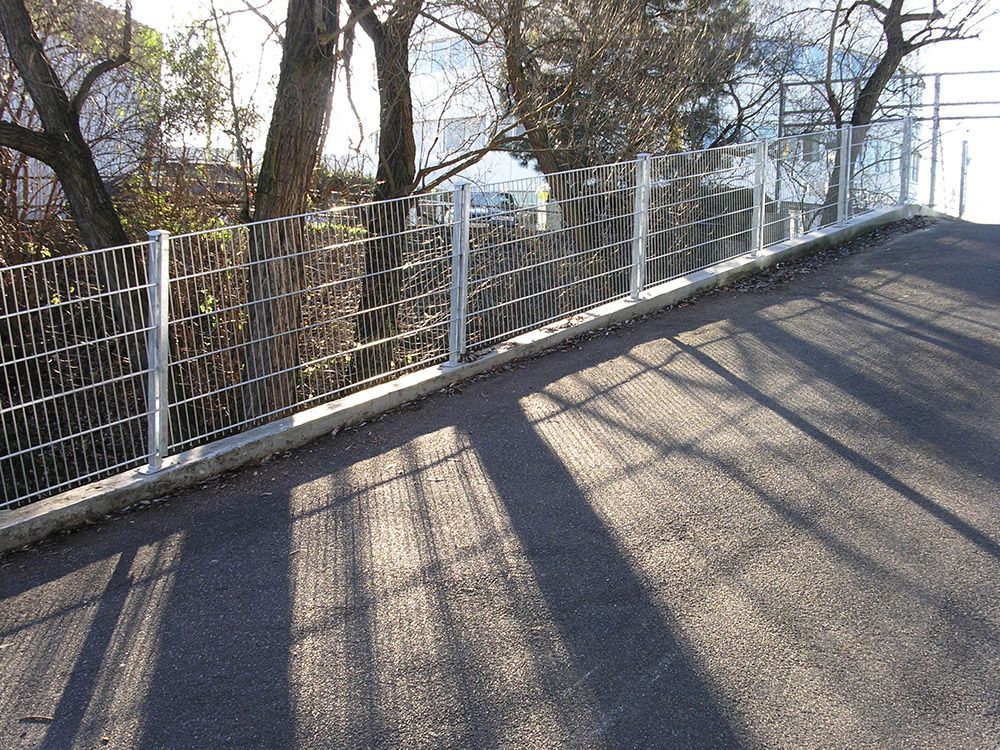 Ein Zaun am Straßenrand mit Bäumen im Hintergrund
