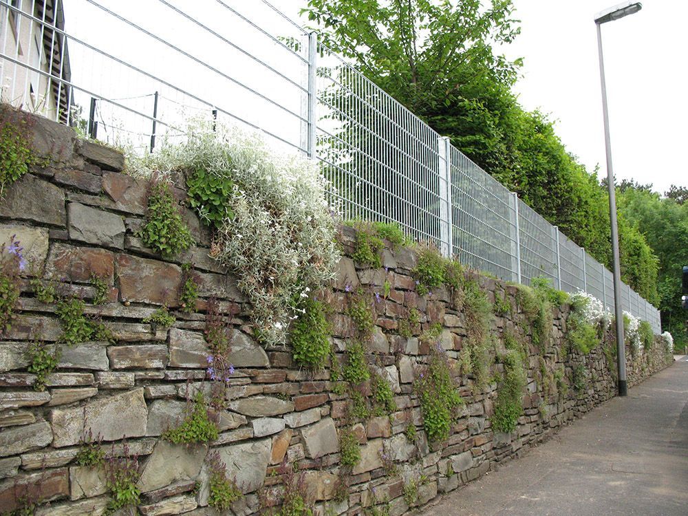 Eine Steinmauer mit einem Stacheldrahtzaun dahinter