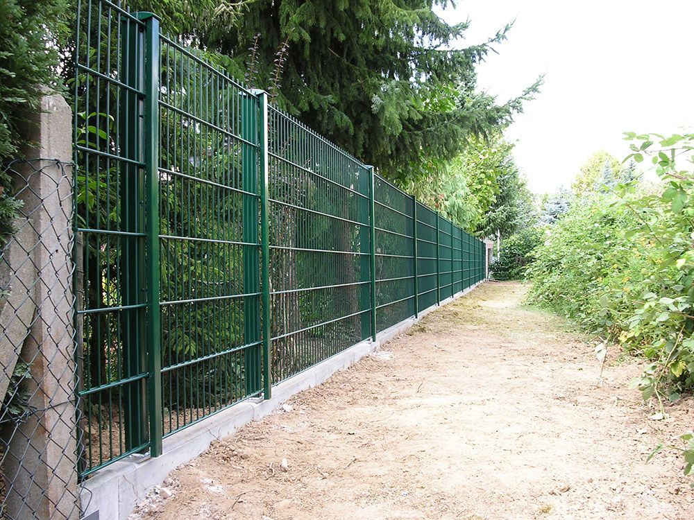 Ein grüner Maschendrahtzaun umgibt einen Feldweg
