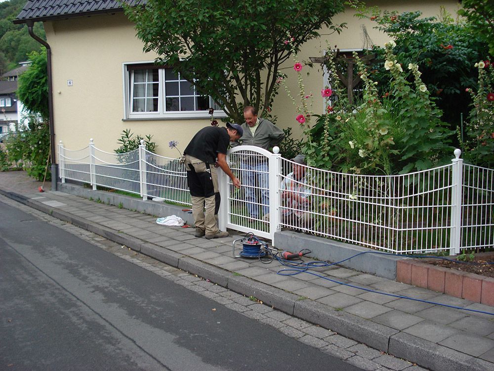 Zwei Männer arbeiten an einem weißen Zaun vor einem Haus