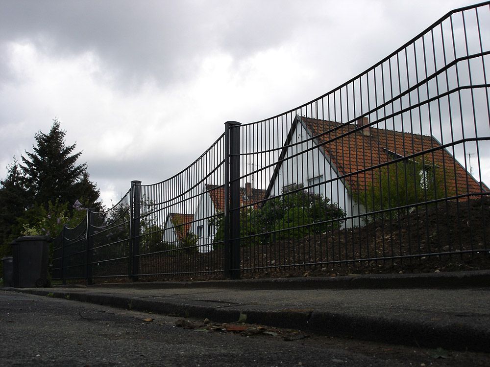 Ein Zaun mit einem Haus im Hintergrund und einem bewölkten Himmel