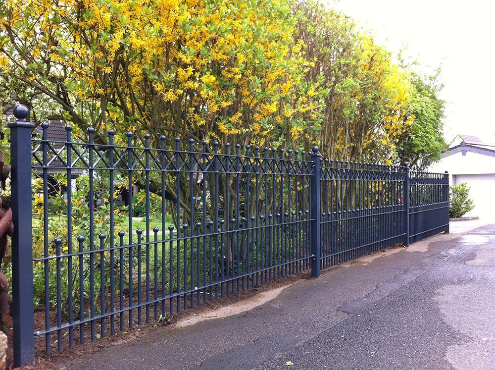 Ein schmiedeeiserner Zaun mit gelben Blumen im Hintergrund
