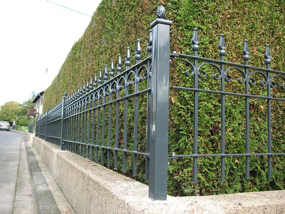 Ein schmiedeeiserner Zaun umgibt eine üppige grüne Hecke