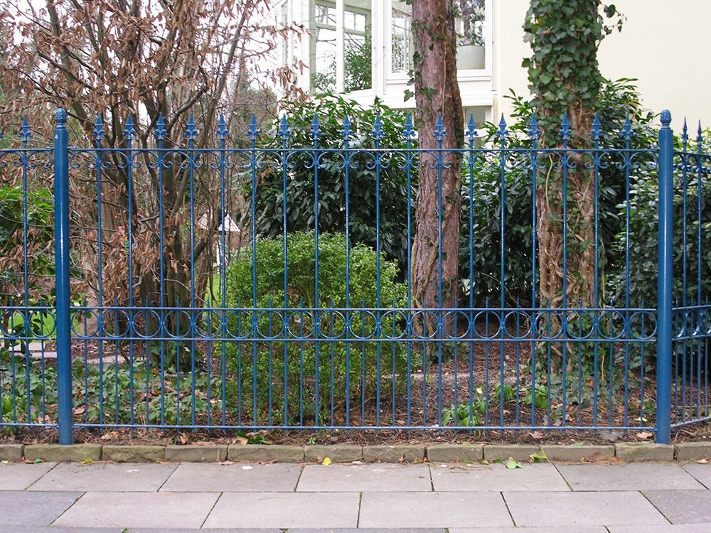 Ein blauer schmiedeeiserner Zaun mit Bäumen im Hintergrund