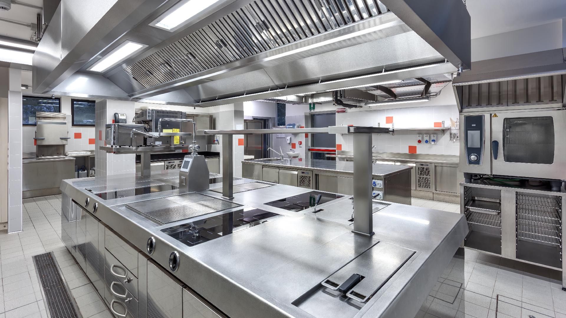 Gastronomieeinrichtungen Gewerbliche Edelstahlküche mit Herden, Arbeitsflächen, Backöfen und Deckenlüftung in einem hellen Arbeitsbereich
