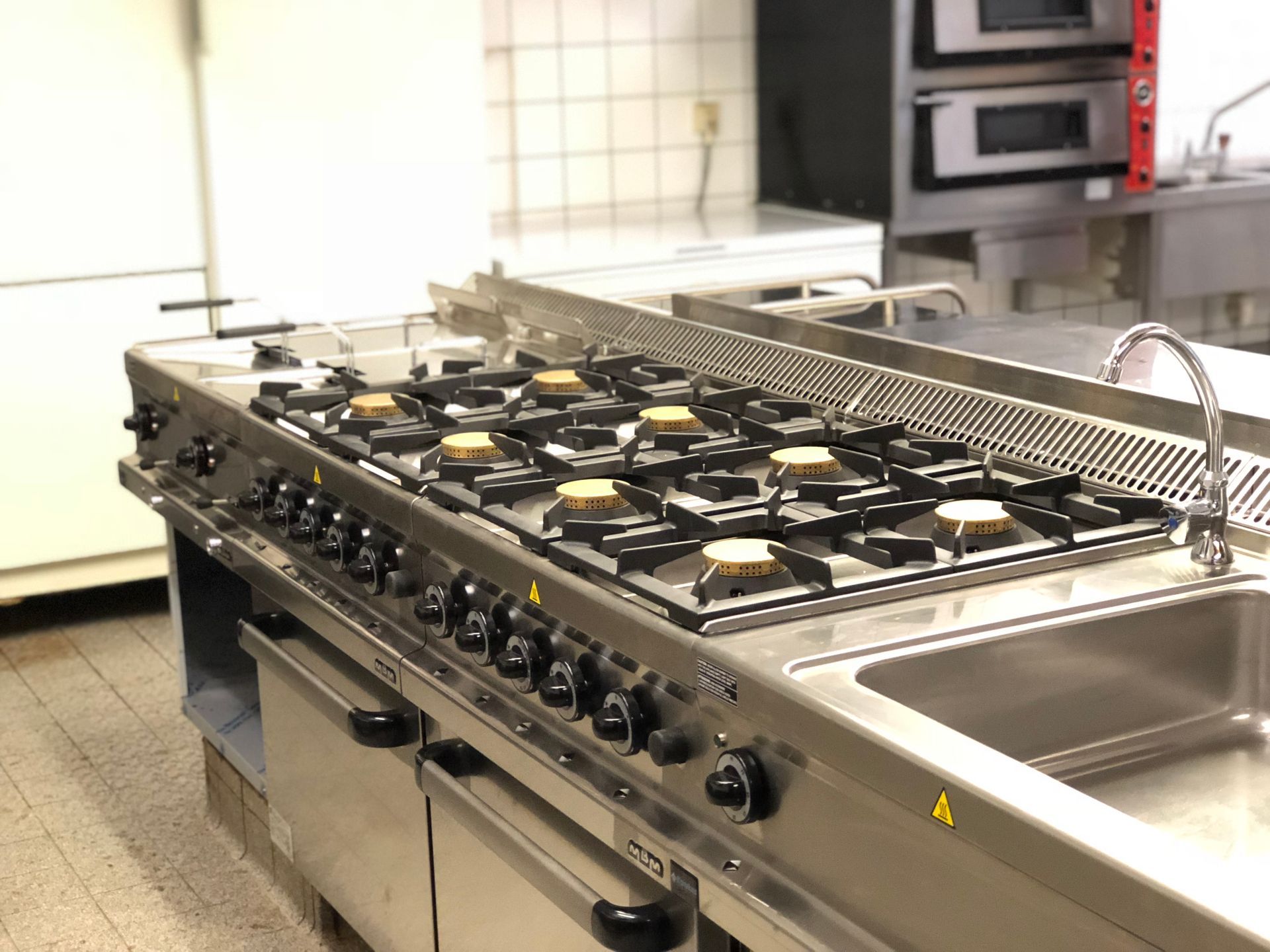 Gewerblicher Küchenherd und Spülbecken mit Arbeitsplatten aus Edelstahl und mehreren Gasbrennern.