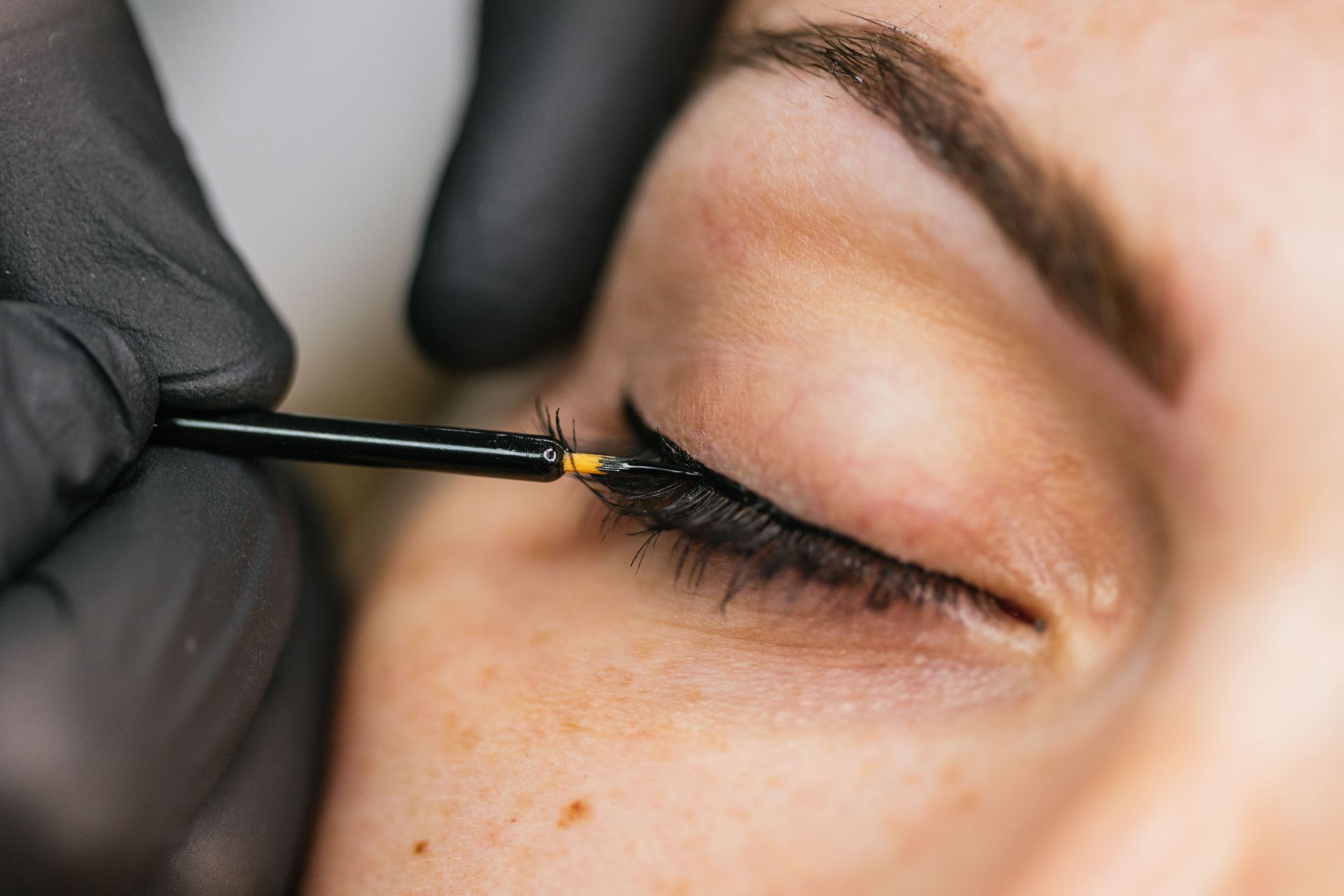 Un primer plano de una persona aplicando delineador de ojos en el ojo de una mujer.