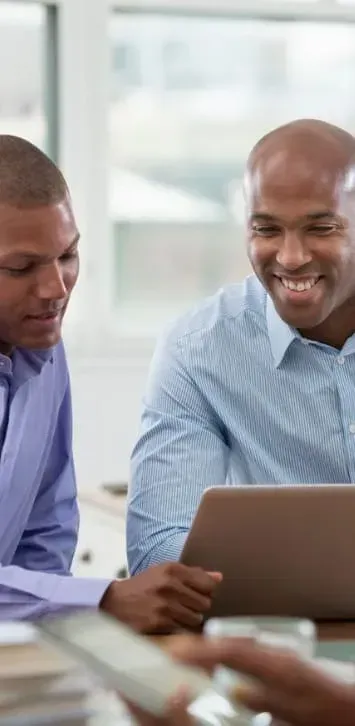 Two men are sitting at a table looking at a tablet computer.